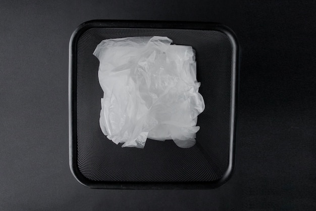 Пластиковый пакет с ручками и перчатками в мусорном ведре на черном фоне Использованный пластиковый пакет для переработки Концепция экологии загрязнение планеты пластиковым целлофановым полиэтиленом