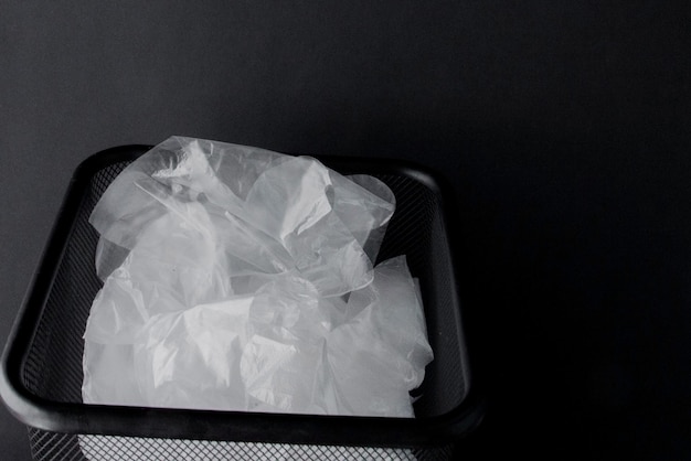 Plastic bag with handles gloves in the bin on a black background Used plastic bag for recycling Concept ecology planet pollution with plastic cellophane polyethylene