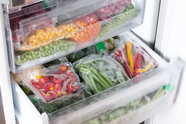 Пластиковые пакеты с различными замороженными овощами в холодильнике. Хранение продуктов