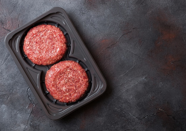 Plastic bakje met rauwe rundergehakt hamburgers met kruiden en specerijen. Bovenaanzicht en.