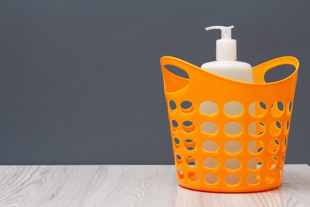 Plastic basket with bottle of dishwashing liquid on gray background with copy space. Washing and cleaning concept.