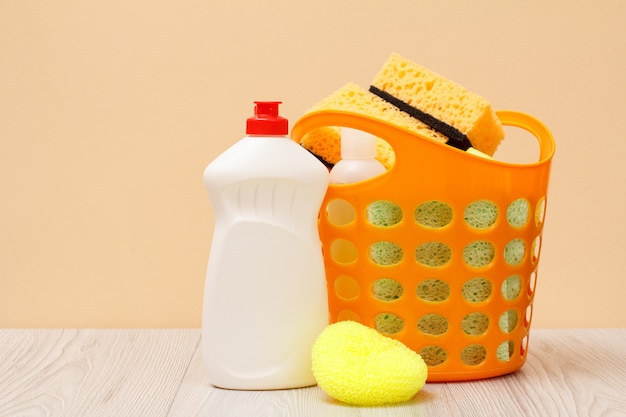 Plastic basket with protective glove, bottles of dishwashing liquid, glass and tile cleaner, detergent for microwave ovens and stoves, sponges on beige background. Washing and cleaning concept.