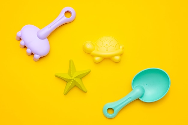 黄色の背景にプラスチックのビーチおもちゃのパステルカラー。細かい運動の概念の開発。創造性ゲームと夏のコンセプトの上面図
