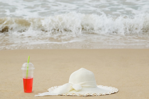 Plastic beker met een rode verfrissing en de hoed met brede rand op het strand