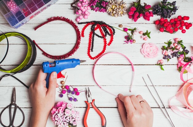 Plastic berries, flowers, beads and instruments for doing handmade headbands. Top view with hands