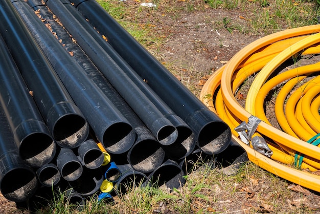 Plastic black pipes lying on the ground next to a roll of yellow cable