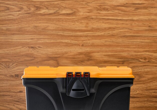 Photo plastic black tool box with yellow cover on a wooden background copy space for text