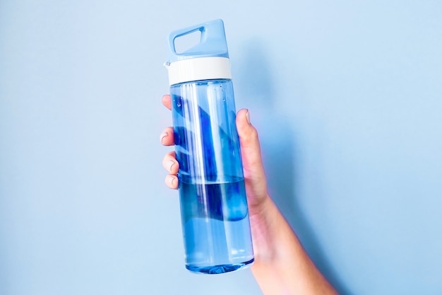 Plastic blue bottle for water in a female hand.