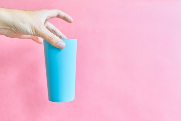 Plastic blue cup in hand on pink background.