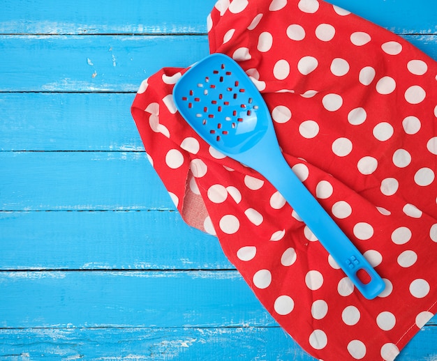 Plastic blue spoon with holes on a red textile napkin