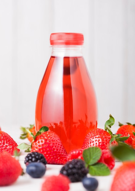 Plastic bottle of berries soda juice drink on wooden background with fresh strawberries and raspberries