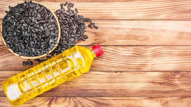 Plastic bottle of cooking oil with bowl of sunflower seeds on wooden background Space for text