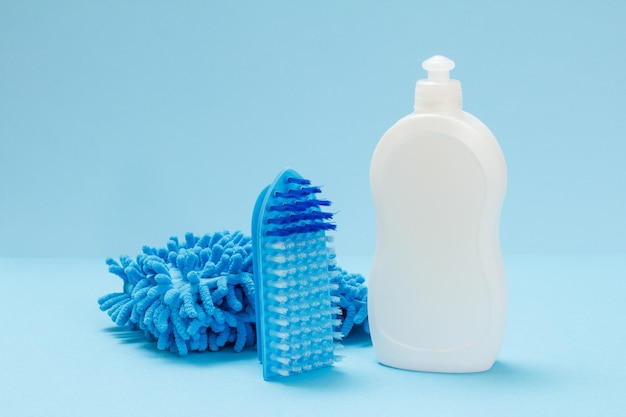 Plastic bottle of dishwashing liquid a rag and a brush on the blue background