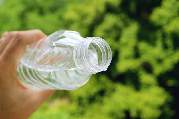 Plastic bottle of drinking water in man's hand with blurry green foliage in background