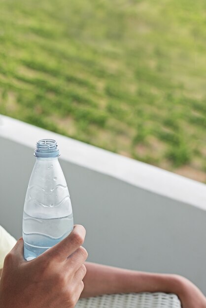 手に水のペットボトル。バルコニーの男は水を飲む