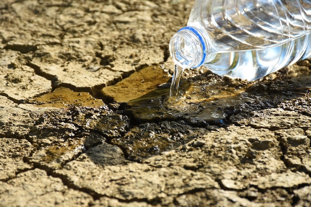 Plastic bottle of water pouring on the cracked soil