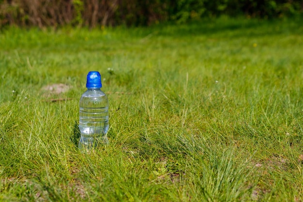 Plastic bottle with fresh drinking water in green grass on meadow