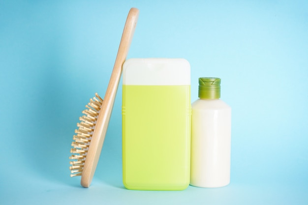 Bottiglie di plastica per la cura del corpo e una spazzola per capelli in legno su sfondo blu.