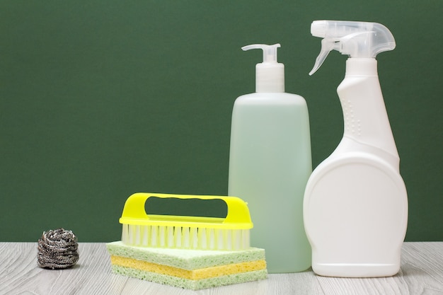 Plastic bottles of detergent for microwave ovens and stoves, glass and tile cleaner, brush and sponges on laminate flooring and green background. Washing and cleaning concept.