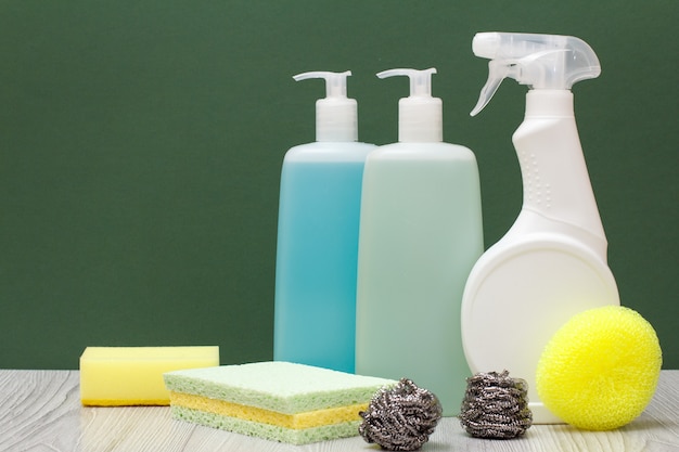 Plastic bottles of detergent for microwave ovens and stoves, glass and tile cleaner and sponges on green background. Washing and cleaning concept.