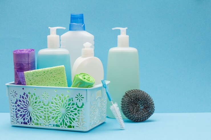 Photo plastic bottles of dishwashing liquid, glass and tile cleaner in basket, sponges, garbage bags on blue background. washing and cleaning concept.