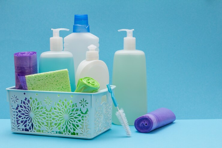 Photo plastic bottles of dishwashing liquid, glass and tile cleaner in basket, sponges, garbage bags and brushes on blue background. washing and cleaning concept.