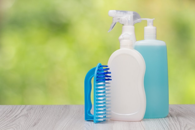 Plastic bottles of dishwashing liquid, glass and tile cleaner, brush on the blurred natural background. Washing and cleaning concept.