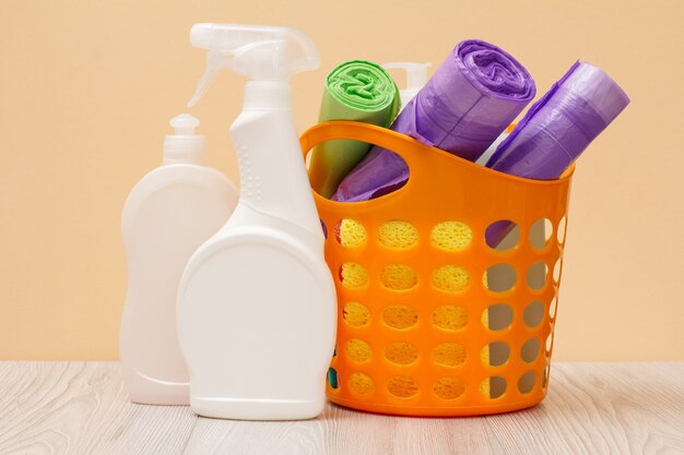 Plastic bottles of dishwashing liquid, glass and tile cleaner, detergent for microwave ovens and stoves, basket, garbage bags, sponges on beige background. Washing and cleaning concept.