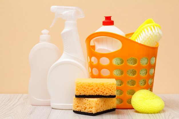 Plastic bottles of dishwashing liquid, glass and tile cleaner, detergent for microwave ovens and stoves, basket, sponges on beige background. Washing and cleaning concept.