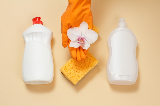Пластиковые бутылки жидких губок для мытья посуды и белый цветок орхидеи на руке в резиновой перчатке