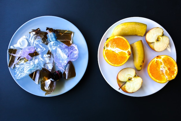 Plastic bottles and fruit on the plate. Life choice. People eating polluted food. Environmental issue. Ecological disaster. Recycling problem. Hands with knife and fork.