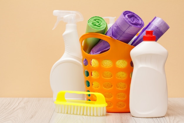 Plastic bottles of glass and tile cleaner, basket with garbage bags, brush on beige background. Washing and cleaning concept.