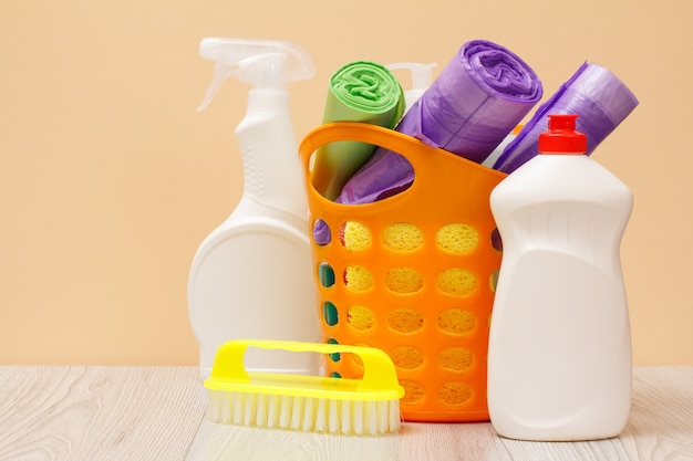 Photo plastic bottles of glass and tile cleaner, basket with garbage bags, brush on beige background. washing and cleaning concept.