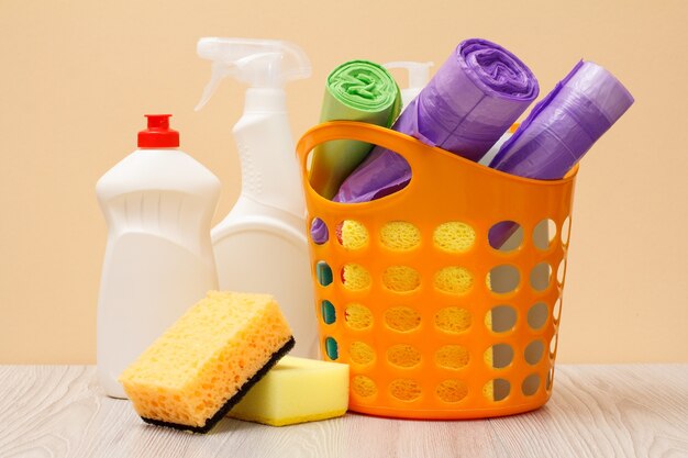 Plastic bottles of glass and tile cleaner, basket with garbage bags, brush, sponges on beige background. Washing and cleaning concept.