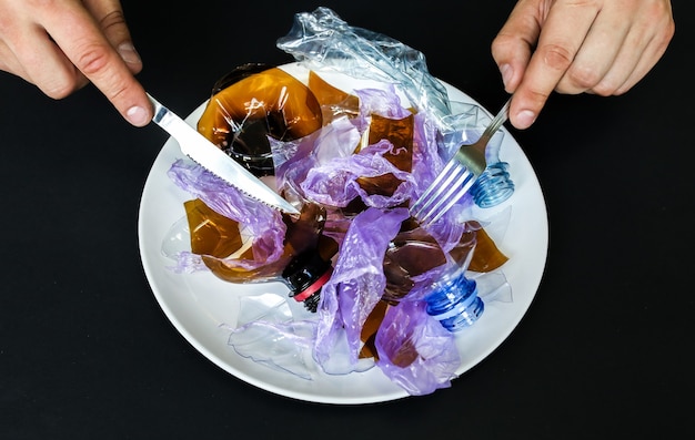 Plastic bottles on the plate. People eating polluted food. Environmental issue. Ecological disaster. Recycling problem. Hands with knife and fork.