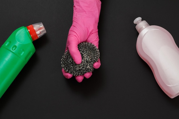 Plastic bottles of washing liquid and a hand with a metal sponge on the black background