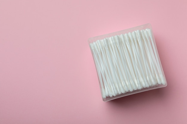 Plastic box with cotton swabs on pink background