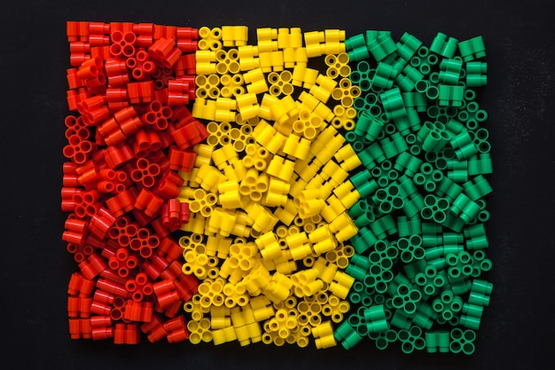 Plastic bricks of red, yellow and green on a black background. Details of toys. Top view.