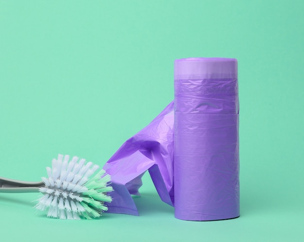 Plastic brush and skein of purple plastic trash bags with\
strings on a green background