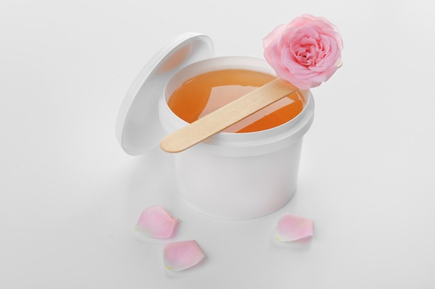 Plastic bucket with sugaring paste, stick and flower on white