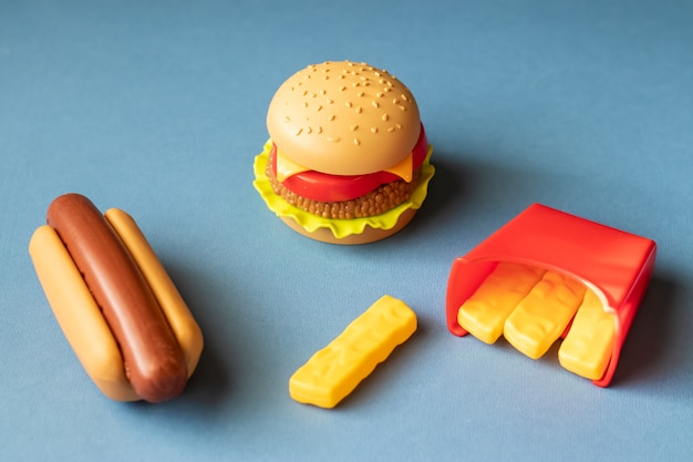 Plastic burger, salad, tomato, frying potatoes with a hot dog on a blue background