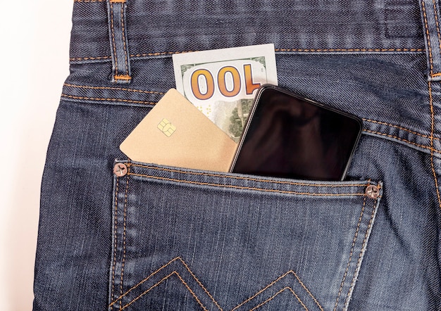 Фото Пластиковая карта, мобильный телефон и наличные в долларах заделывают в кармане джинсов.