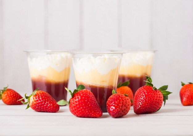 Plastic container with strawberry cream dessert on wooden table with fresh strawberries