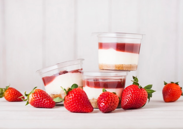 Plastic container with strawberry cream dessert on wooden table with fresh strawberries