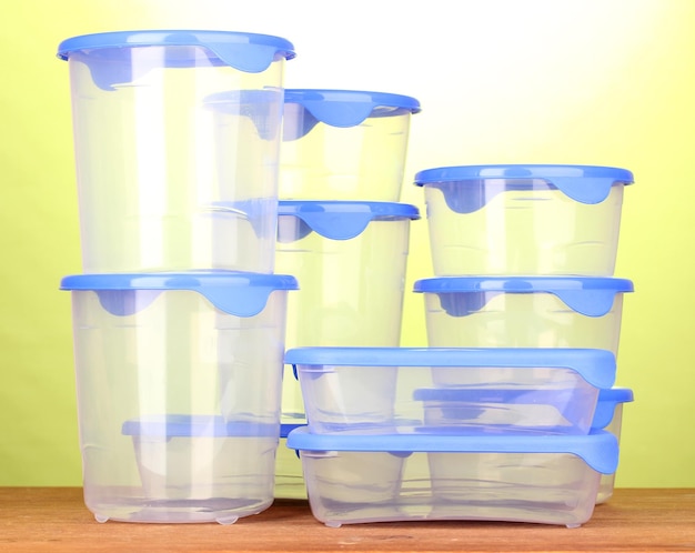 Plastic containers for food on wooden table on green background