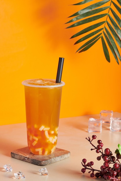 Plastic cup filled with fresh and tasty orange juice on a wooden coaster on the table