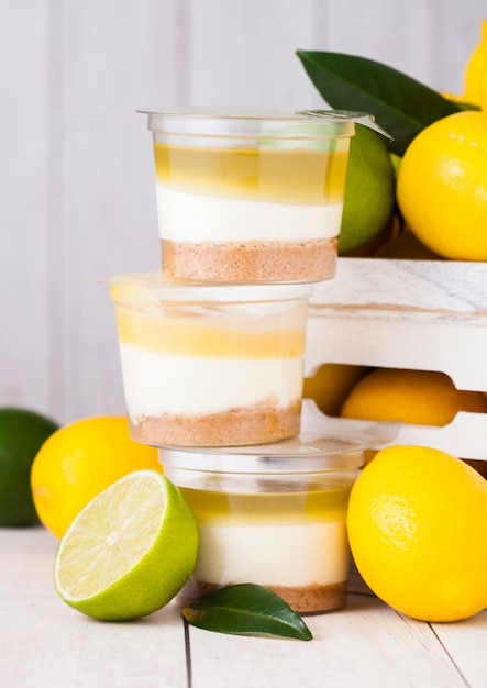 Plastic cup with lemon lime cream and biscuit dessert with raw lemons in white wooden box