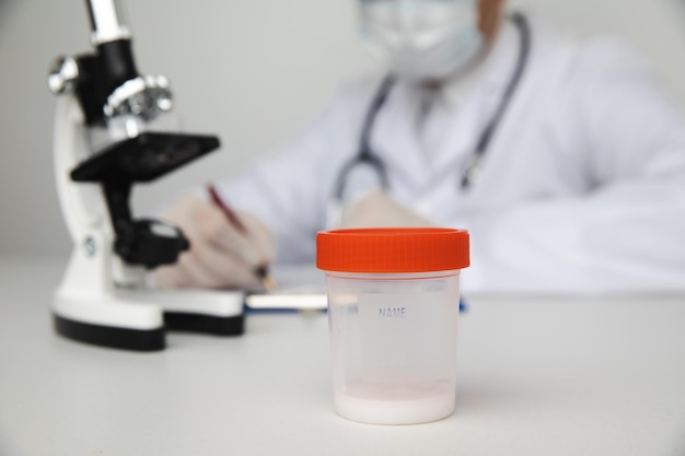 医者のテーブルのクローズアップで精液分析のための精子が入ったプラスチック製のコップ