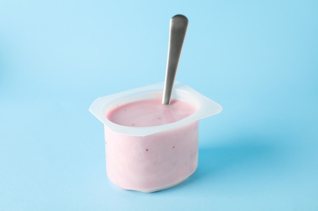 Photo plastic cup with yogurt and spoon on color background,