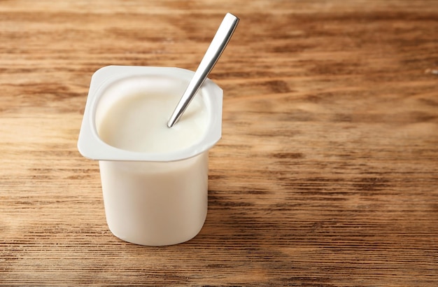 Фото Пластиковая чашка с вкусным йогуртом на деревянном фоне